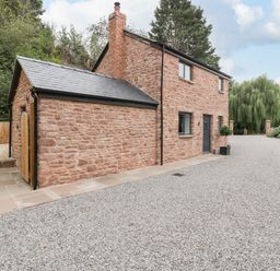 A stone house with a black door and windows surrounded by gravel and trees at The Old Mill Bake House in Goodrich
