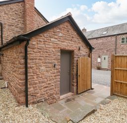A stone building with a closed grey door and an open wooden gate on a gravel and stone patio at The Old Mill Bake House in Goodrich