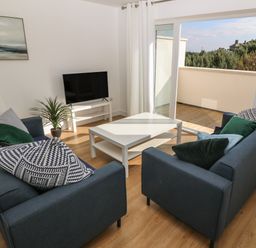A living room with two blue sofas a white coffee table a television on a stand a floor lamp a plant and sliding glass doors leading to a balcony at 3 Lon Y Dryw in Trearddur Bay