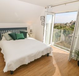 A bedroom with a bed green pillows bedside tables lamps and an open glass door leading to a balcony at 3 Lon Y Dryw in Trearddur Bay