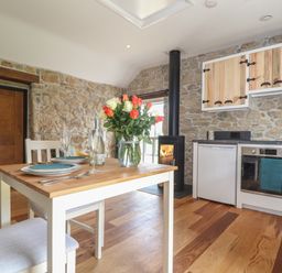 A kitchen and dining area with a wooden table set for two and stone walls at The Hayloft in Helston
