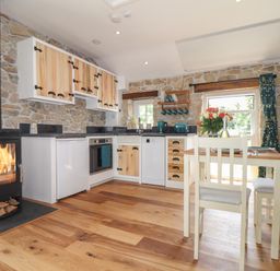 A kitchen with stone walls a wood burning stove wooden cabinets and a dining table with chairs at The Hayloft in Helston