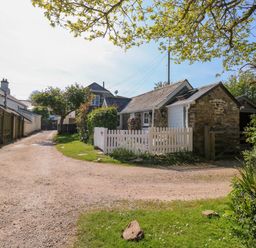 A gravel driveway leading to stone and white cottages with a white picket fence and greenery at Toad Hall Cottage Hutcherleigh near Blackawton