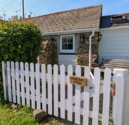 A white picket fence with a wooden sign in front of a small stone cottage at Toad Hall Cottage Hutcherleigh near Blackawton