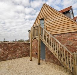 An exterior view of a brick building with wooden cladding and an outdoor wooden staircase at Coach House Mews in Alderminster