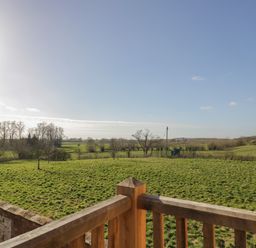A view of green fields with trees and a wooden railing in the foreground at Coach House Mews in Alderminster