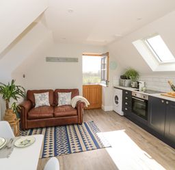 A kitchen with black cabinets a brown leather sofa and a wooden door at Coach House Mews in Alderminster