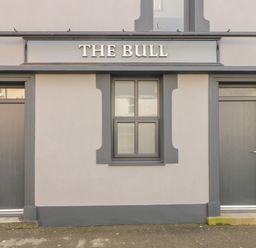 The exterior of a building with two grey doors and a window under a sign that reads THE BULL at The Bull Inn in Deiniolen