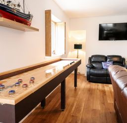A game room with a shuffleboard table black leather chair brown leather sofa wall mounted TV and model ship on shelf at The Bull Inn in Deiniolen