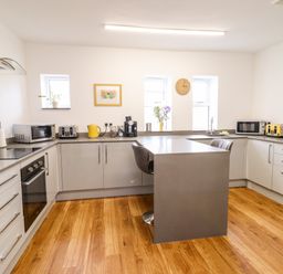 A kitchen with an island and two chairs a microwave a toaster a coffee maker and a clock on the wall at The Bull Inn in Deiniolen