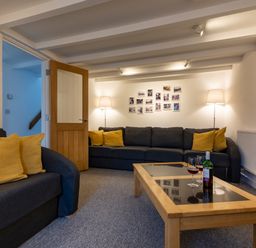A seating area with two dark sofas with yellow cushions a wooden coffee table with wine glasses and bottle and lamps at Rose Cottage in St Ives