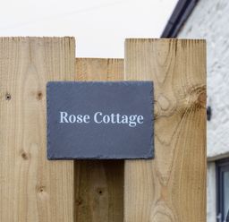A wooden fence with a dark rectangular sign that reads Rose Cottage at Rose Cottage in St Ives