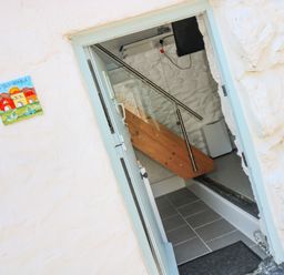 An entryway with a door open showing a stairway with metal handrails inside a white stone building at The Old Stable in Porthallow