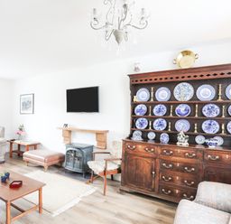 A living room with a wooden cabinet displaying blue and white plates and brass candlesticks at Bryn Afon Farm in Llanrug