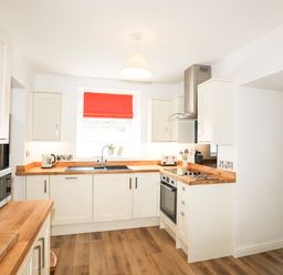 A kitchen with white cabinets wooden countertops a microwave and a red window blind at Bryn Afon Farm in Llanrug