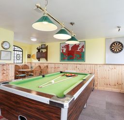 A room with a pool table billiard cues and balls a dartboard a table with four chairs and framed pictures on yellow walls at Bryn Afon Farm in Llanrug