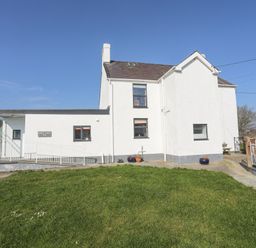 A white two-story house with a sloped roof and grass in front at Bryn Afon Farm in Llanrug