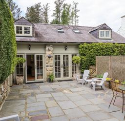 A stone patio with outdoor chairs and tables outside a cottage with dormer windows at Garden Cottage in Garndolbenmaen near Tremadog