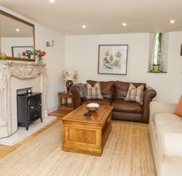 A living room with a brown leather sofa, beige sofa, wooden coffee table, decorative fireplace, and floral artwork at Garden Cottage in Garndolbenmaen near Tremadog