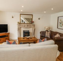 A living room with a beige sofa a brown leather sofa a wooden coffee table a TV on a wooden stand and a fireplace with a mirror above at Garden Cottage in Garndolbenmaen near Tremadog