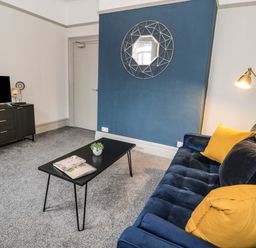 A living room with a blue sofa yellow cushions black coffee table and a wall-mounted mirror at Sapphire Suite in Barmouth