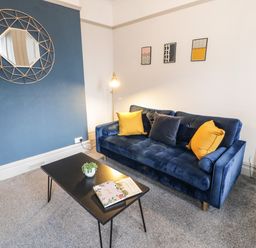 A living room with a blue sofa with cushions and a black coffee table with a plant and book at Sapphire Suite in Barmouth