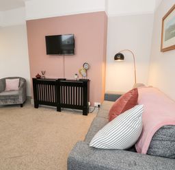 A living room with a gray sofa, cushions, a gray armchair, a wall-mounted TV, and a black cabinet at Rose Suite in Barmouth