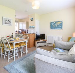 A living room with a grey sofa a dining table with chairs and a small kitchen area at The Nook in Mundesley