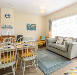 A dining table with four chairs and a sofa with cushions in a living room at The Nook Mundesley
