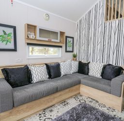 A living room with a gray sectional sofa with black and white cushions a patterned floor and wallpaper at Hares Rest Nantmel near Rhayader