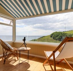 A sunroom with two chairs a small round table and a telescope overlooking the sea and hillside at Ocean View in Downderry