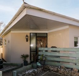 The entrance of a single-story house with a wooden door and three small windows by a light hanging on the wall at Ocean View in Downderry