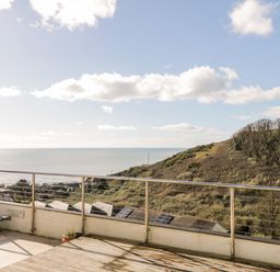 A balcony with railing and a lounge chair overlooking a hill and the sea at Ocean View in Downderry