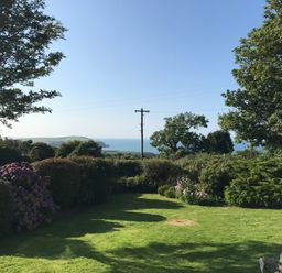 A garden with grass, bushes, trees, and a view of the sea at Penllain Newport Pembrokeshire