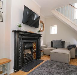 A living room with a grey sofa a black fireplace and a wall-mounted TV at Rydal Cottage in Scarborough