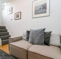 A beige sofa with gray and black cushions next to carpeted stairs and framed pictures on the wall at Rydal Cottage in Scarborough