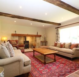 A living room with two sofas a wooden coffee table a red patterned rug exposed wooden beams a fireplace and a window with curtains at Morgans Farmhouse Bampton Oxfordshire