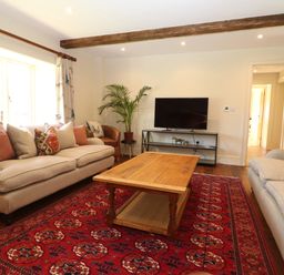 A living room with sofas a wooden coffee table a red patterned rug a television on a stand and a potted plant at Morgans Farmhouse in Bampton Oxfordshire
