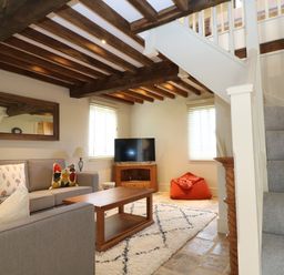 A living room with grey sofas a wooden coffee table TV on a wooden stand an orange bean bag a rug and carpeted stairs at Morgans Farmhouse in Bampton Oxfordshire
