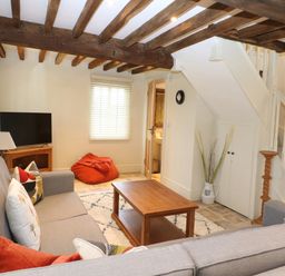 A living room with exposed wooden beams a gray sofa a wooden coffee table a television and a bean bag at Morgans Farmhouse in Bampton Oxfordshire