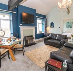 A living room with two black leather sofas a glass dining table set with plates and glasses a wall mounted tv and a fireplace at The Stable in Lydney