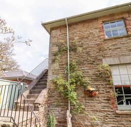 An outdoor stone staircase next to a brick building with two windows and climbing plants at The Stable in Lydney