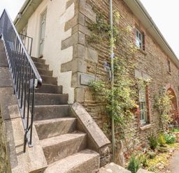 Stone staircase with black metal railing next to a stone and brick building with plants along the wall at The Stable in Lydney