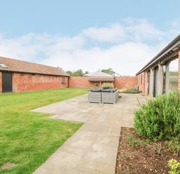 An outdoor patio with seating and umbrella between two red brick buildings at Shorthorn Barn in Attlebridge near Taverham