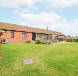 A lawn with patio furniture and a barbecue near a brick building at Shorthorn Barn in Attlebridge near Taverham