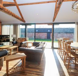A living room with leather sofas a wooden dining table with chairs wooden beams and a brick wall at Shorthorn Barn in Attlebridge near Taverham