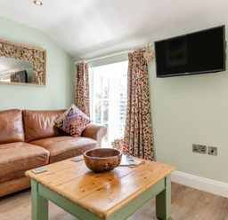 A living room with a brown leather sofa a wooden coffee table a wall mounted tv and patterned curtains at Armando in Devoran Cornwall
