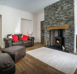 A living room with a stone fireplace leather sofas red cushions and a white rug at Fellside Lodge in Bowness-On-Windermere