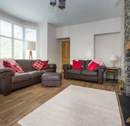 A living room with two brown leather sofas red cushions a stone fireplace and wooden floor at Fellside Lodge in Bowness-On-Windermere