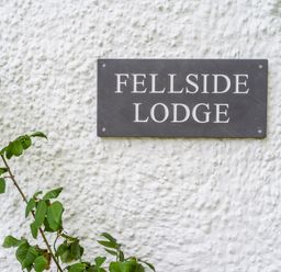 A sign reading Fellside Lodge on a textured white wall with green leaves on the side at Fellside Lodge in Bowness-On-Windermere
